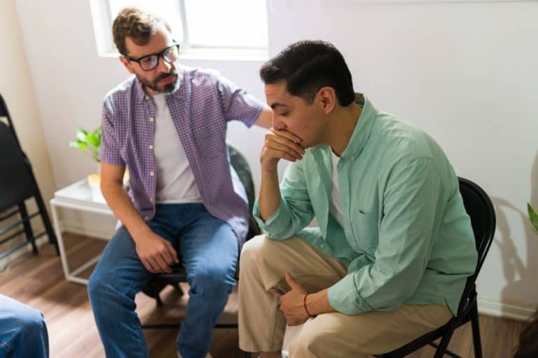 Man showing empathy, comforting his sad friend during a support group meeting, focusing on mental health and recovery