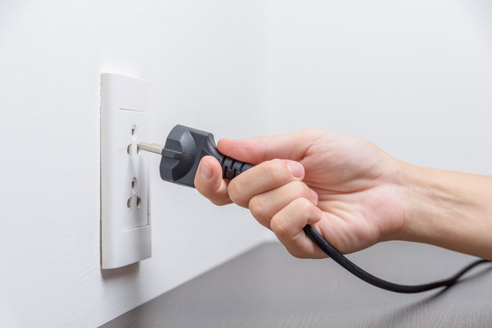 Female hand inserting a black electrical plug into outlet. Closeup view of a fork and a socket.