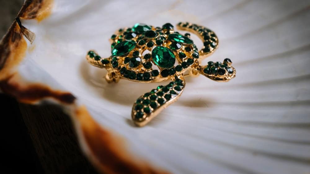 Veroli, Italy - 19-11-2025: Elegant turtle-shaped brooch with emerald-green stones resting on a large seashell — stylish gemstone fashion accessory.