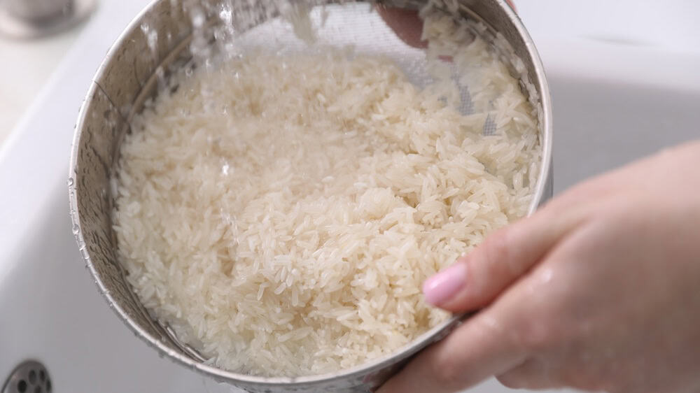 Woman washing rice in sieve at sink, closeup