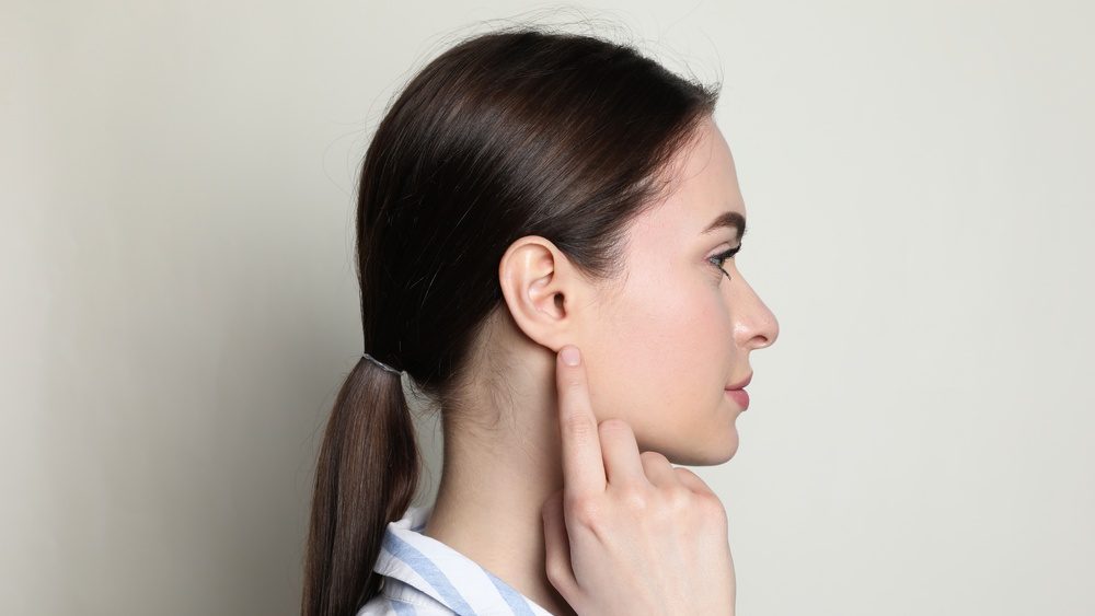 Young woman pointing at her ear on light background