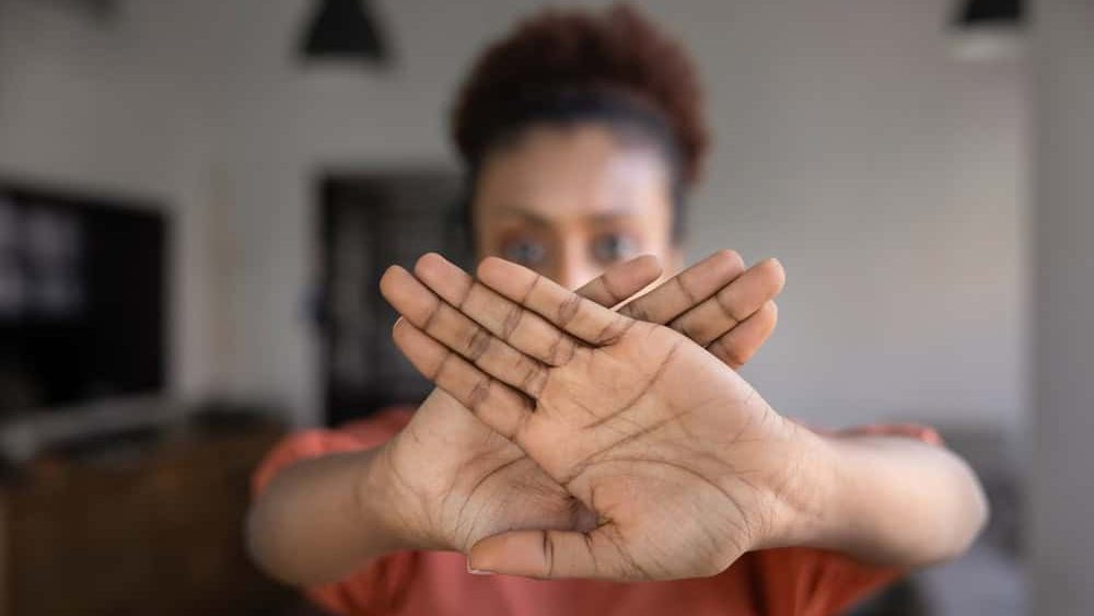Anxious serious young African American woman making stop gesture with both hands, showing crossed palms at camera, saying no to abuse, discrimination, expressing protest, ban