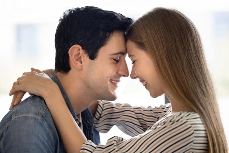 Close up photo of young affectionate couple hugging indoors, touching their foreheads gently, smiling with eyes closed, enjoying tender moment, feeling love, expressing deep connection. Relationships