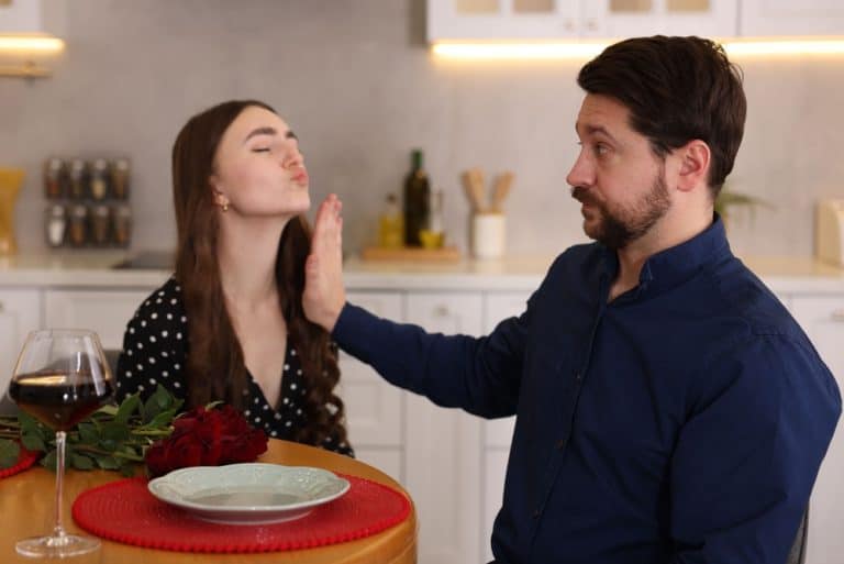 Bad date. Embarrassed man refusing kiss from woman at table during dinner indoors