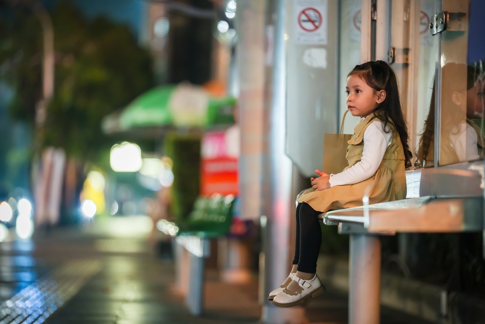 Little child girl waiting for bus at bus stop in Bangkok city street at night, Thailand