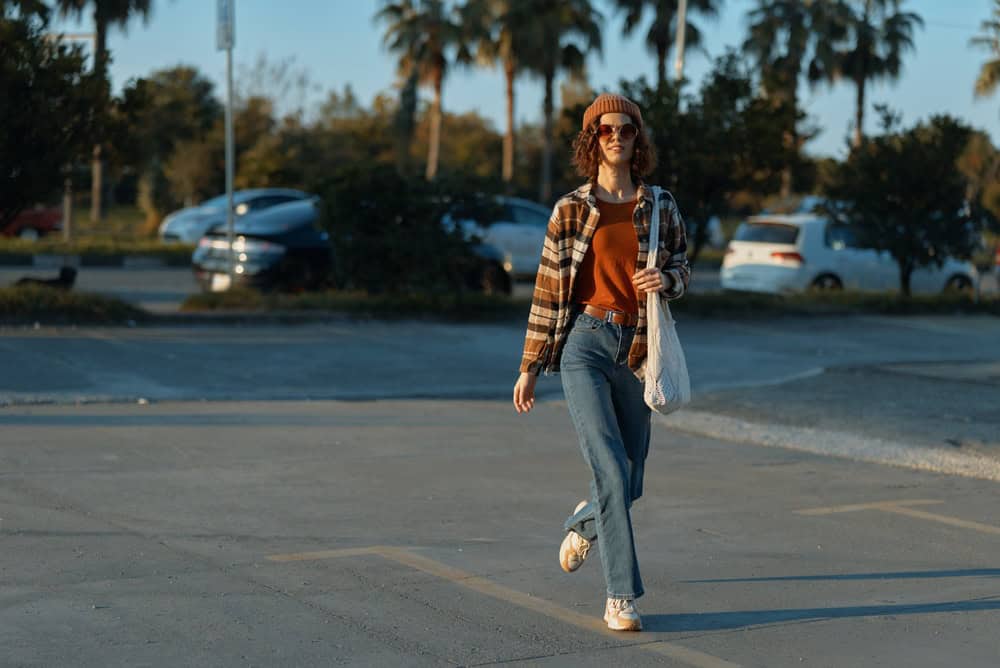 woman walking candid in urban parking at golden hour with authenticity and casual style, wearing jeans, jacket and tote bag; smiling, mindful living mood with emotional storytelling glow