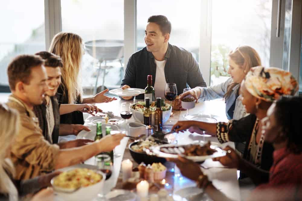People, friends and dining with food in home for celebration, social gathering or feast together. Group, community or eating with alcohol, dinner or meal for thanksgiving or festive bonding in house