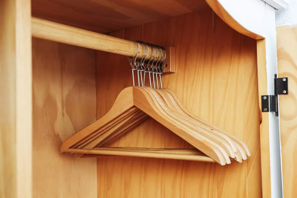Wooden hangers in wardrobe closet. Empty clothes hangers on rail inside cabinet. Storage space for clothing in home interior. Organization of wardrobe with wooden hangers.