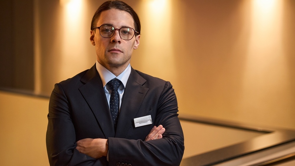 Portrait of young adult Caucasian hotel administrator wearing name badge, standing with crossed arms and looking at camera, conveying leadership and service for corporate branding