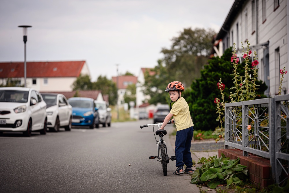 Serious young boy looking over shoulder while walking with bicycle on street with copy space