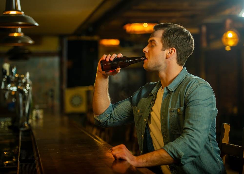 Young man drinking beer from a bottle while relaxing alone at a bar.