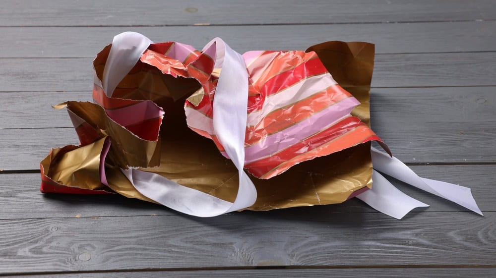 Crumpled torn wrapping paper and ribbon on grey wooden table, closeup