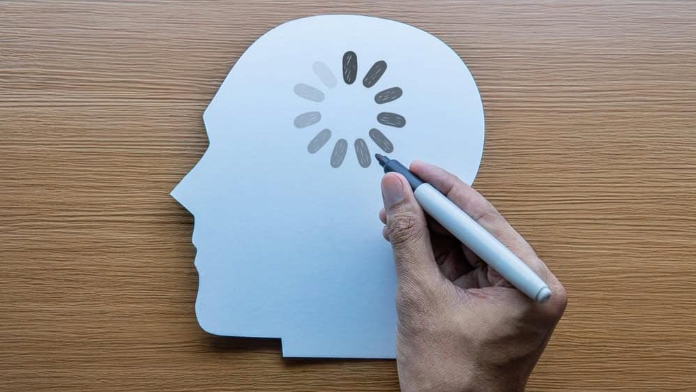 Hand drawing a loading icon onto a white paper human head silhouette. Mental fatigue, brain fog, cognitive delay, slow learning concept.