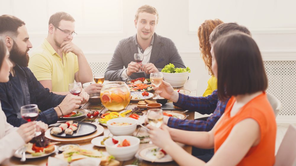 Friends meeting. Group of people drink wine at party dinner table in cafe, restaurant. Young company celebrate with alcohol and food at wooden table indoors.