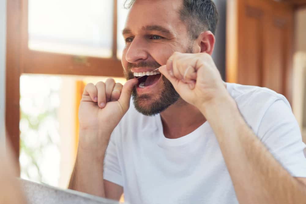 Man, teeth and flossing with morning routine in home for grooming, oral care and hygiene for wellness. Male person, reflection and mouth for dental health, fresh breath and bathroom with confidence