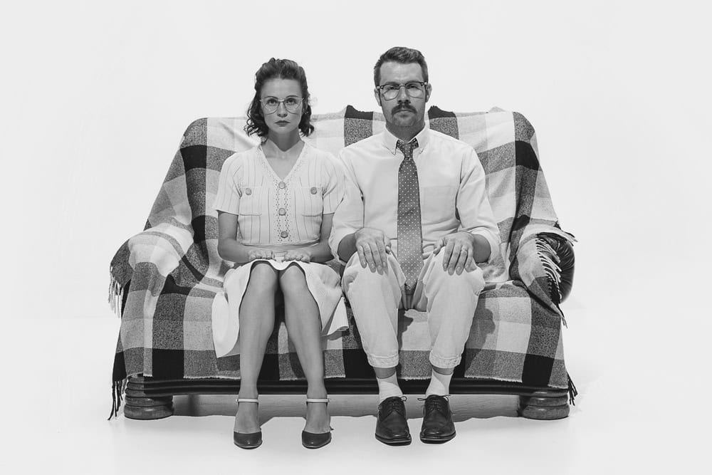 Portrait of serious man and woman sitting on sofa and looking at camera isolated over white background. Concept of love, relationship, retro style, creativity, family. Copy space for ad