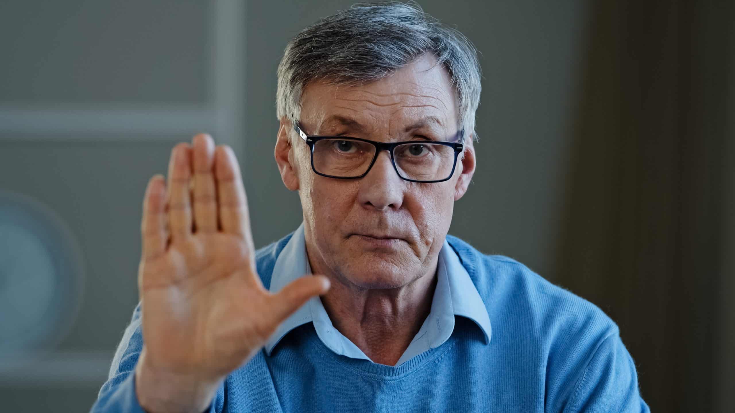 Serious old senior mature 60s man stretch out palm to camera says stop gesture indoors. Social problems older generation disrespect ban refusal disagreement. Aged businessman trouble denial rejection