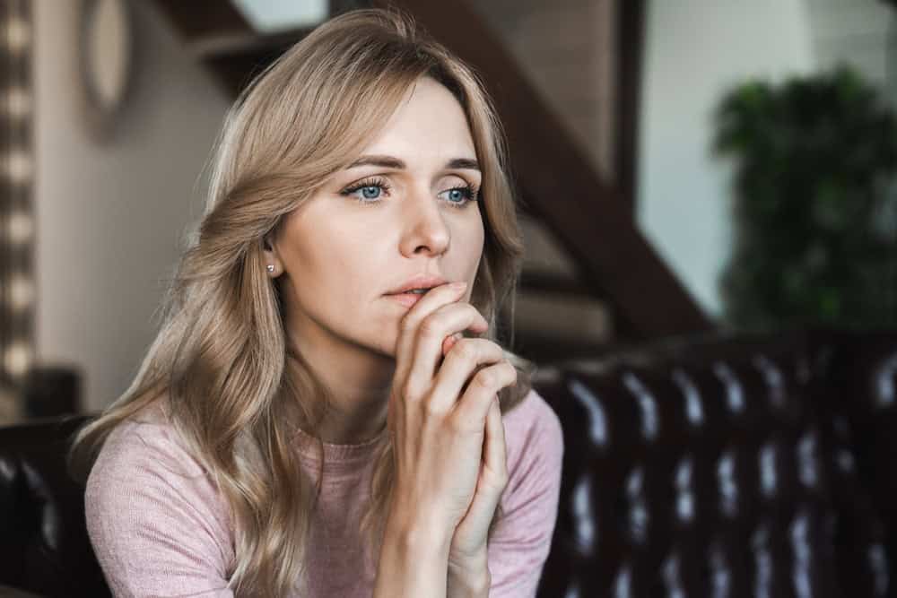 Tired, upset young woman looking worried with her hand at her mouth.