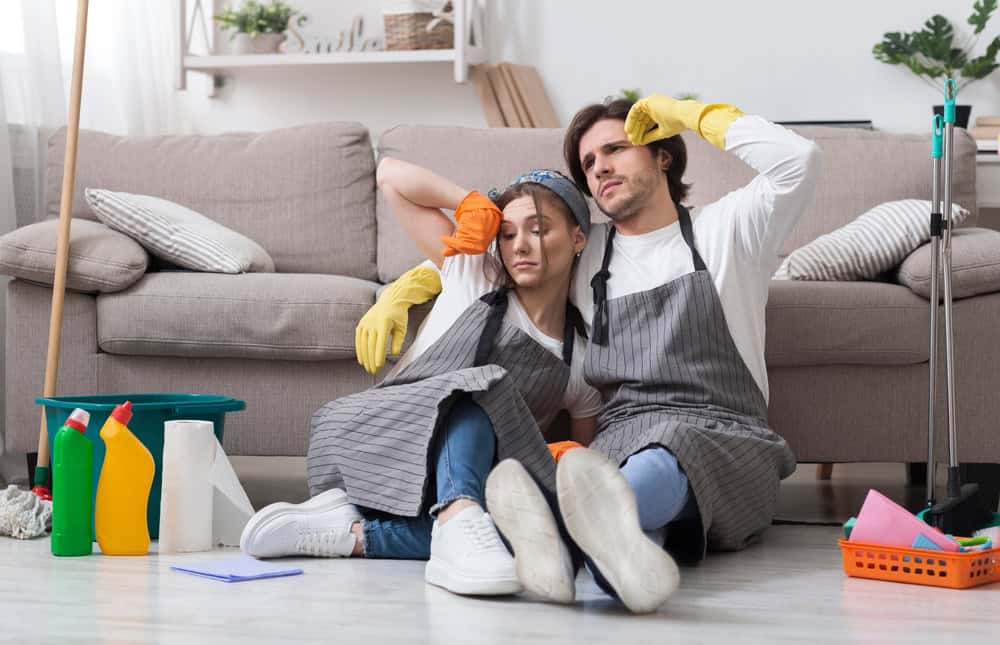 Tired Of Domestic Duties. Portrait Of Exhausted Couple Resting On Floor After Spring-Cleaning Home