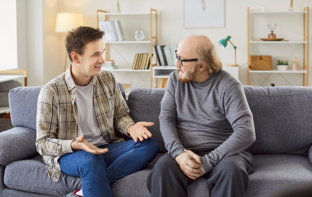 Adult son and a senior father talking. Old man in his 60s sitting on the couch together with his grown up son and listening to him ready to share his life wisdom. Parents and children concept
