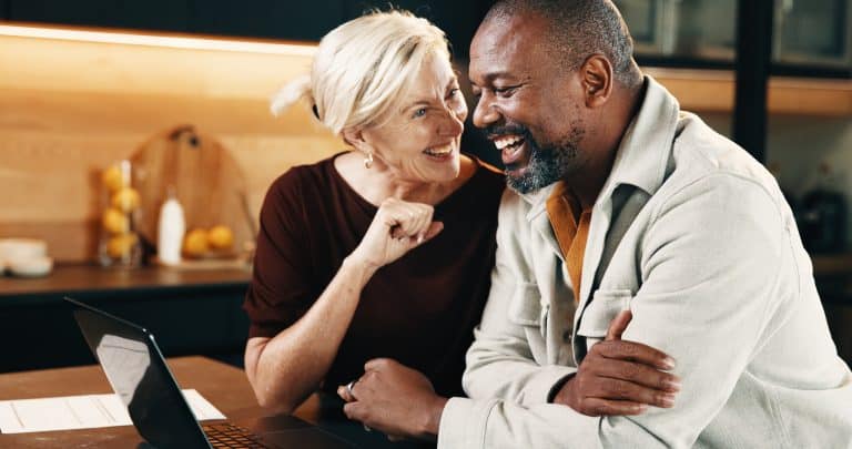 Mature, couple and laugh in home with laptop, funny joke and website for booking holiday together.