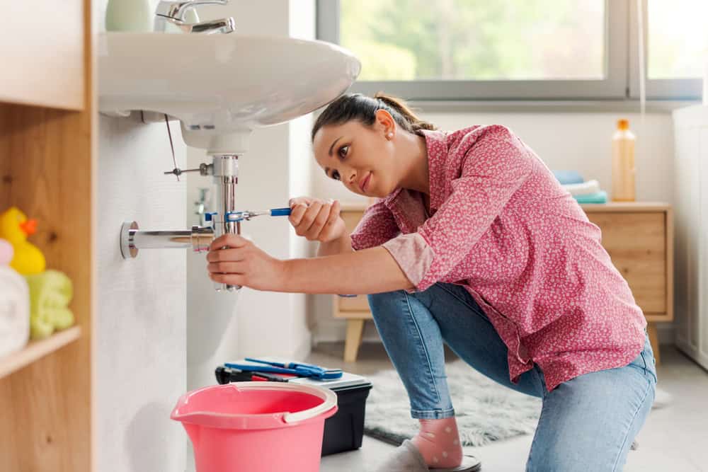 Skilled young woman fixing the bathroom sink by herself using pliers