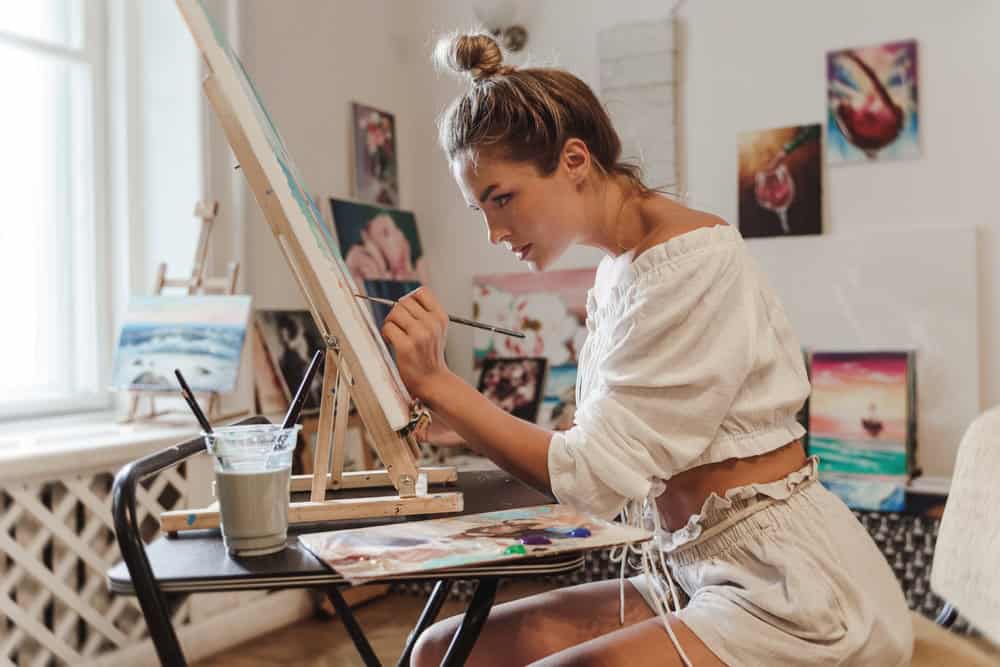 Young,Female,Artist,Is,Painting,On,A,Canvas,In,An