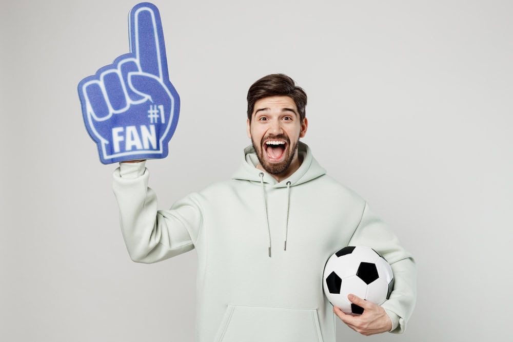 Young excited fun man fan wears mint hoody foam 1 fan glove finger up cheer up support football spor