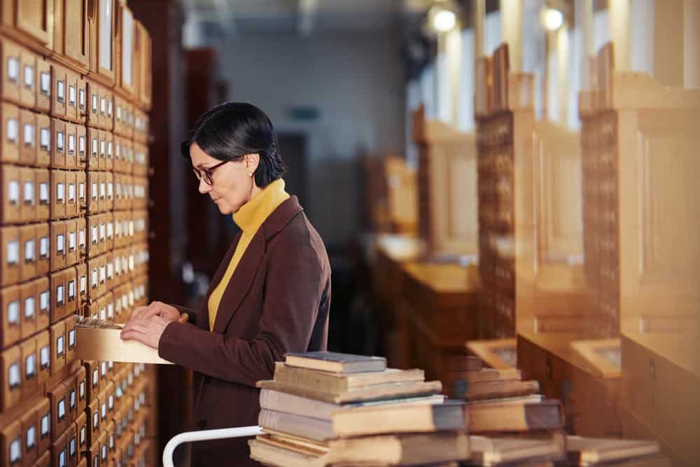 Side view portrait of female librarian organizing library catalogue cabinet