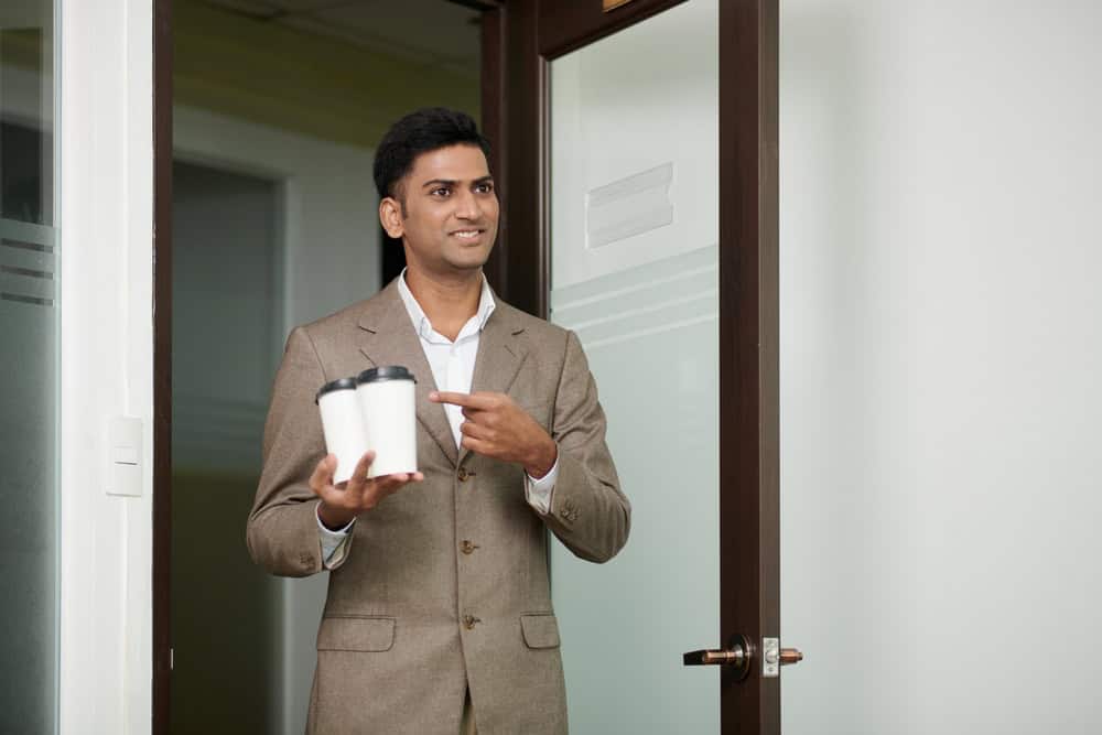Smiling businessman bringing take-out coffee for himself and colleague in the morning