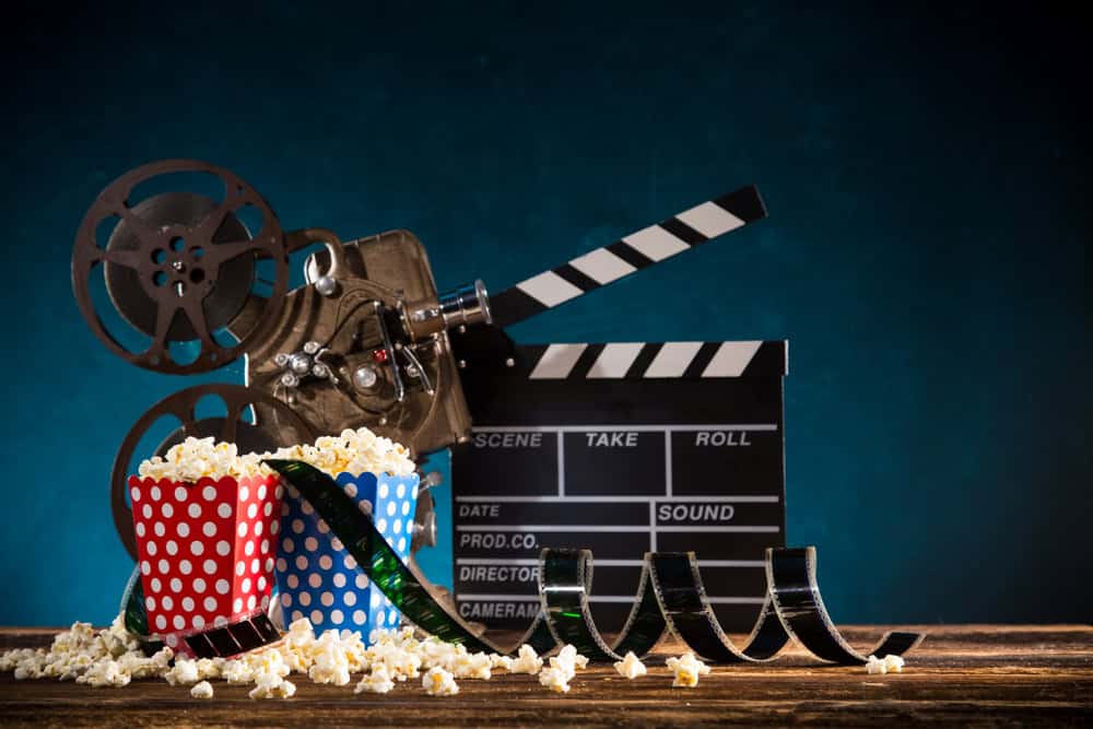 Cinema concept of vintage film reel with popcorn on old wooden background.