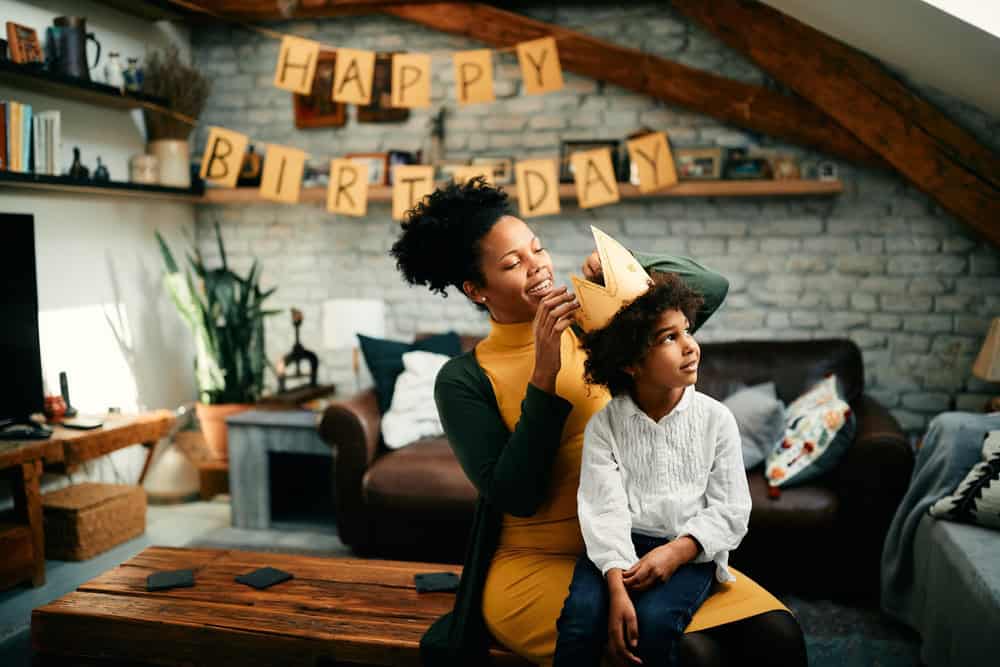 Happy African American mother putting a crown on daughter's head while preparing for Birthday party