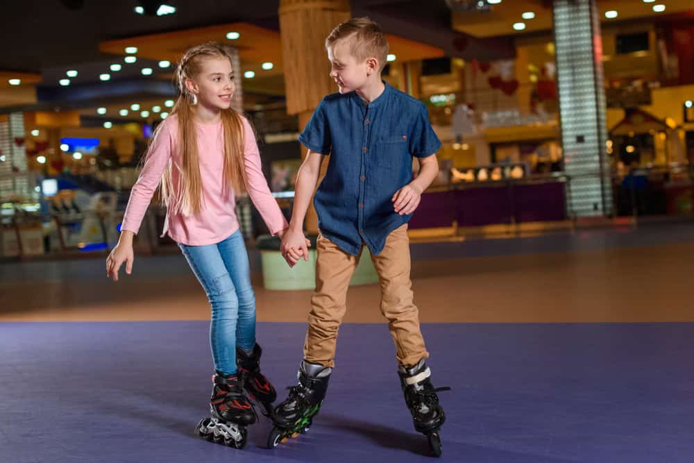 adorable kids holding hands while skating together on roller rink