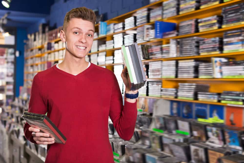 Happy man looking for interesting movies on shelves of CD shop