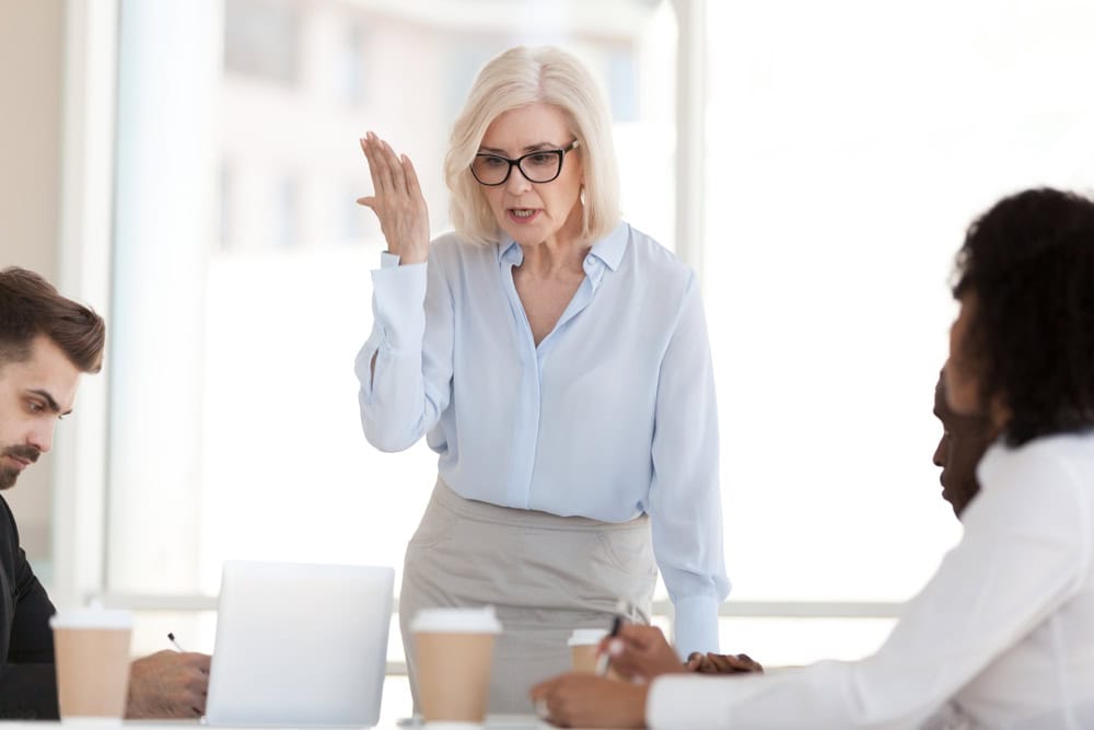 Angry powerful mature businesswoman boss scolding employees frustrated by bad work results in office, dissatisfied female middle aged executive rebuking diverse workers at group corporate meeting