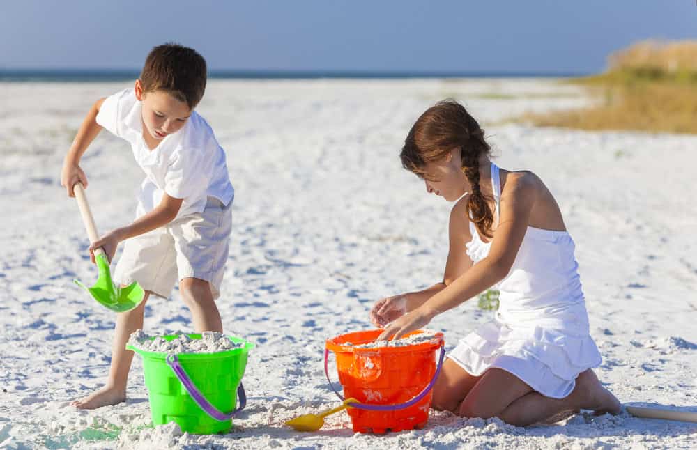 Happy children, boy & girl, brother& sister having fun playing in the sand on a beach with bucket and spade
