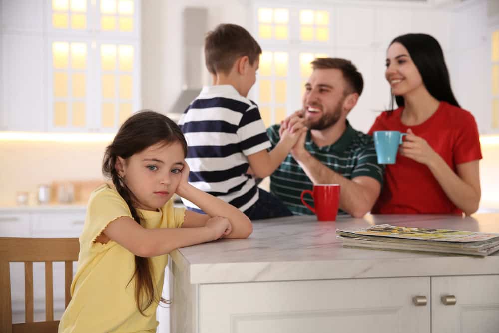 Unhappy little girl feeling jealous while parents spending time with her brother at home