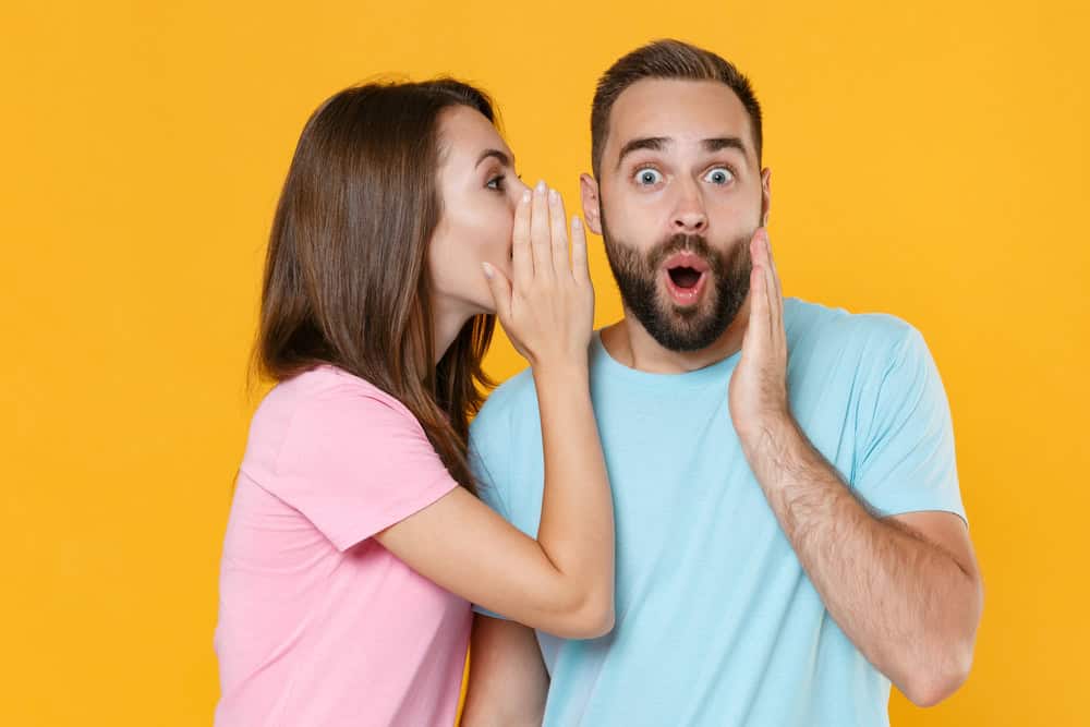 Shocked young couple friends guy girl in blue pink t-shirts isolated on yellow background. People lifestyle concept. Mock up copy space. Whispering secret behind Shocked young couple friends guy girl in blue pink t-shirts isolated on yellow background. People lifestyle concept. Mock up copy space. Whispering secret behind hand, sharing news, put hand on cheek.hand, sharing news, put hand on cheek.