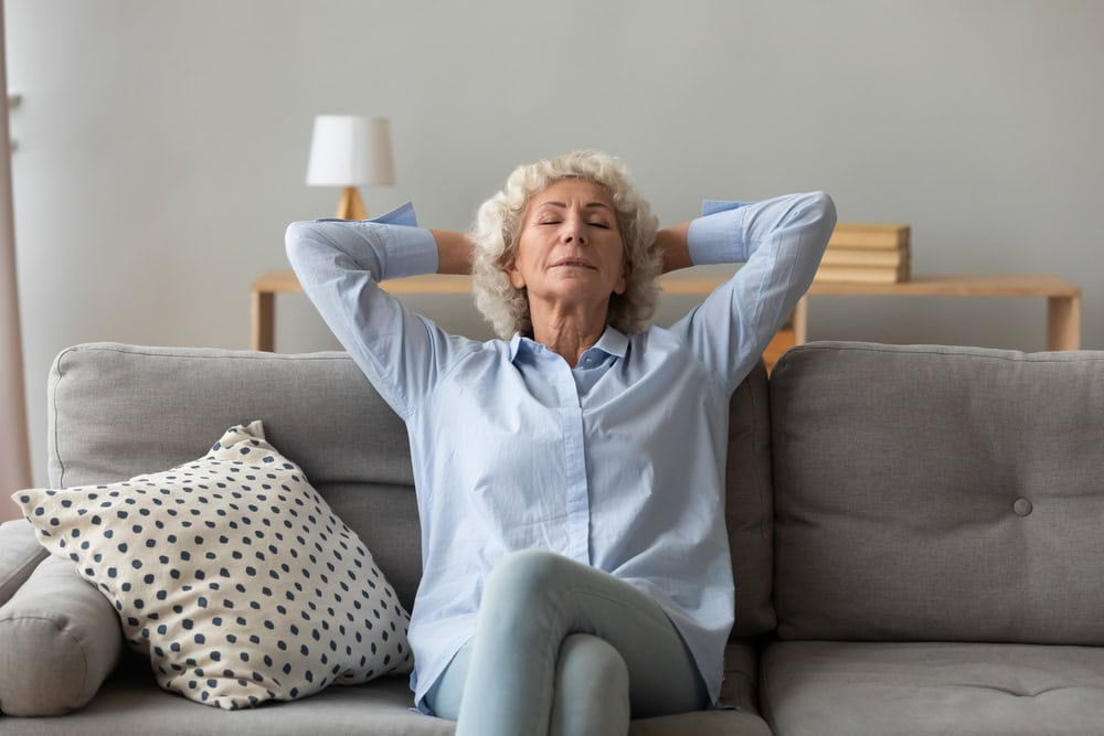 Mindful older mature grandmother sleeping on cozy sofa in modern living room. Happy elderly senior retired 70s grey haired woman relaxing indoors, enjoying peaceful lazy moment alone at home.
