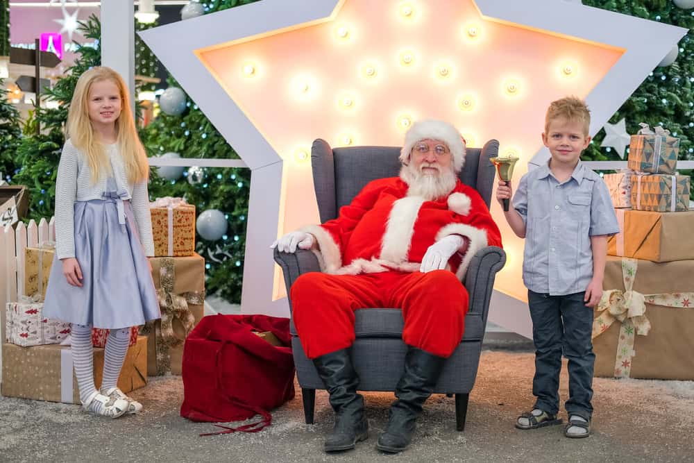 Portrait Santa Claus with kids in Shopping Mall. Brother and sister taking photo with Santa. Christmas sales and wishes.