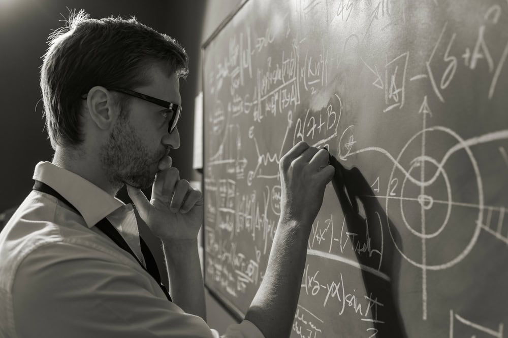 Young smart mathematician drawing math formulas on the chalkboard and thinking: he is solving problems and discovering new theories