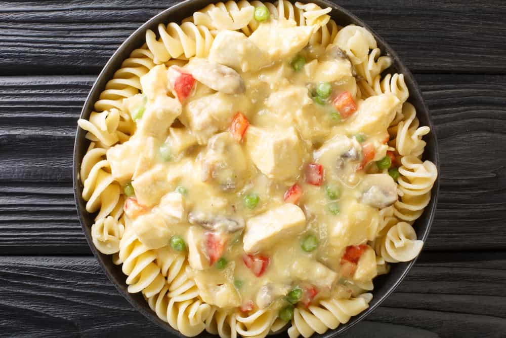 Chicken a la King is tender chicken in a creamy sauce with mushrooms, bell peppers and peas served with pasta close up in the plate on the table. Horizontal top view from above