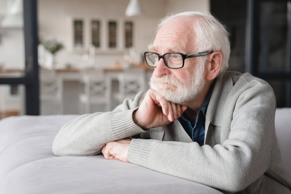 Sad tired ill sick lonely disappointed caucasian old elderly senior man grandfather sitting on the sofa couch, feeling nostalgy, pain, missing grandchildren, bankruptcy, fraud at home