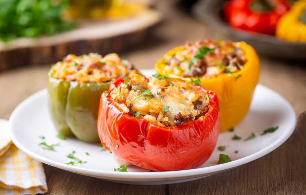 Stuffed peppers, halves of peppers stuffed with rice, dried tomatoes, herbs and cheese in a baking dish on a blue wooden table, top view. (Turkish name; biber dolmasi)