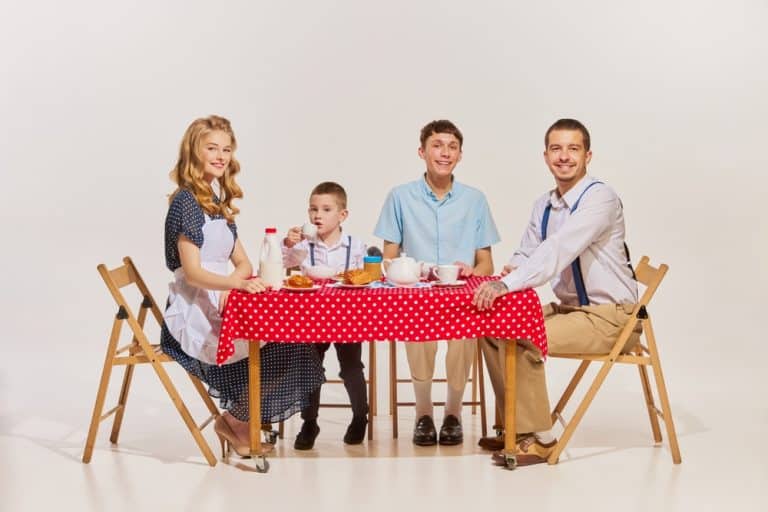 Portrait of lovely young family, woman, man and two boys sitting at the table and having breakfast