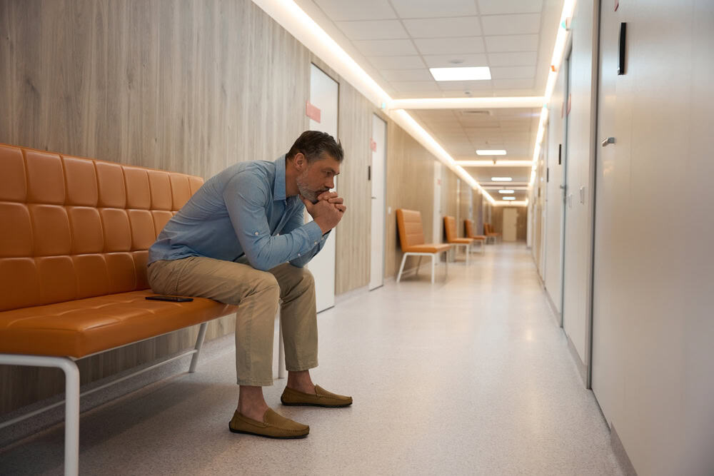 Adult man with beard sits the corridor of modern hospital