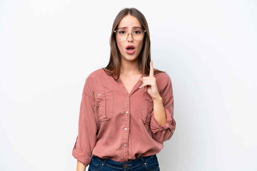Young woman isolated on a white background lifting a finger up as she realizes the solution