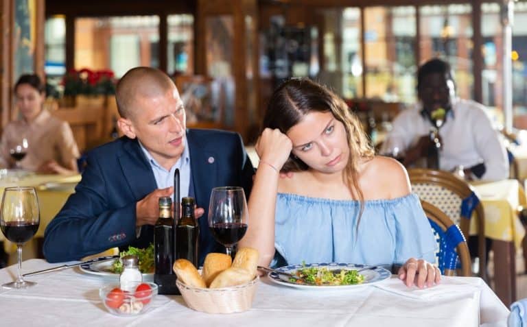 Man complimenting woman at restaurant, she looks annoyed and uncomfortable.