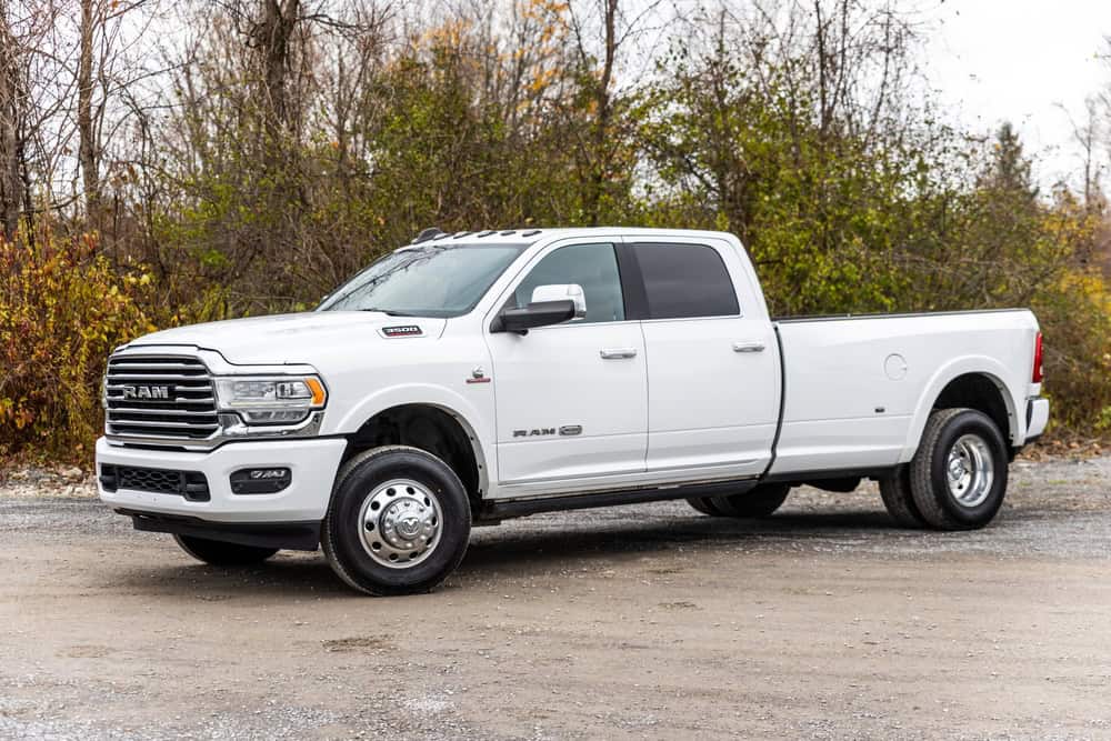 OSWEGO, US - Nov 11, 2023: A white Ram pickup truck sits in a parking area, nestled against a backdrop of wooded terrain