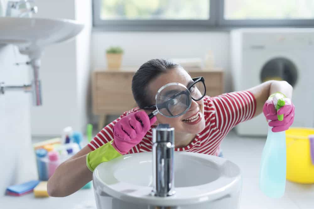 Woman obsessed with hygiene: she is holding a detergent and looking through a magnifying glass